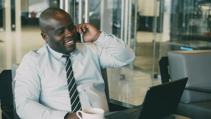 Man talking on phone with coffee and laptop.